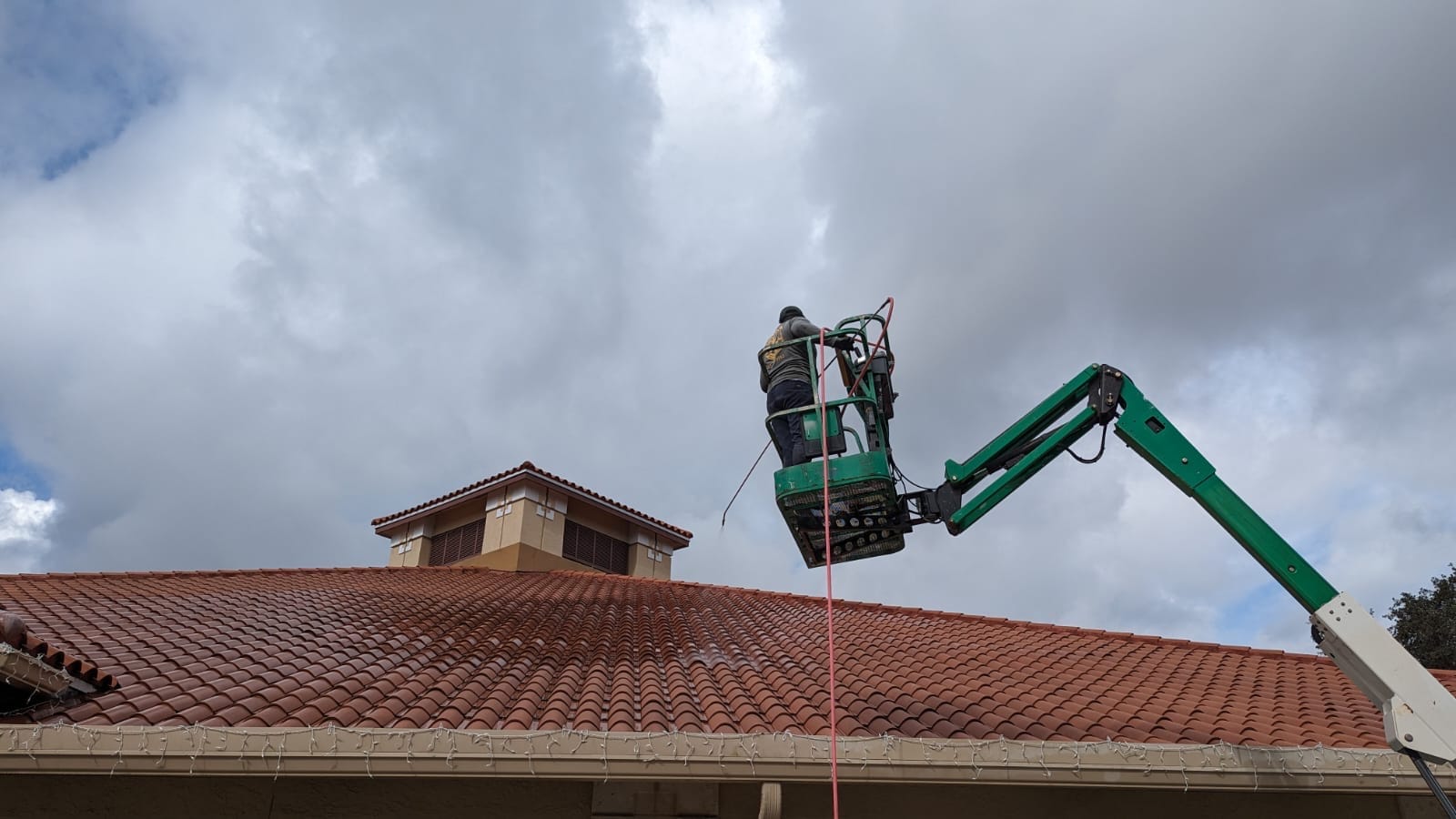 Technician on a boom lift cleaning a commercial tile roof
