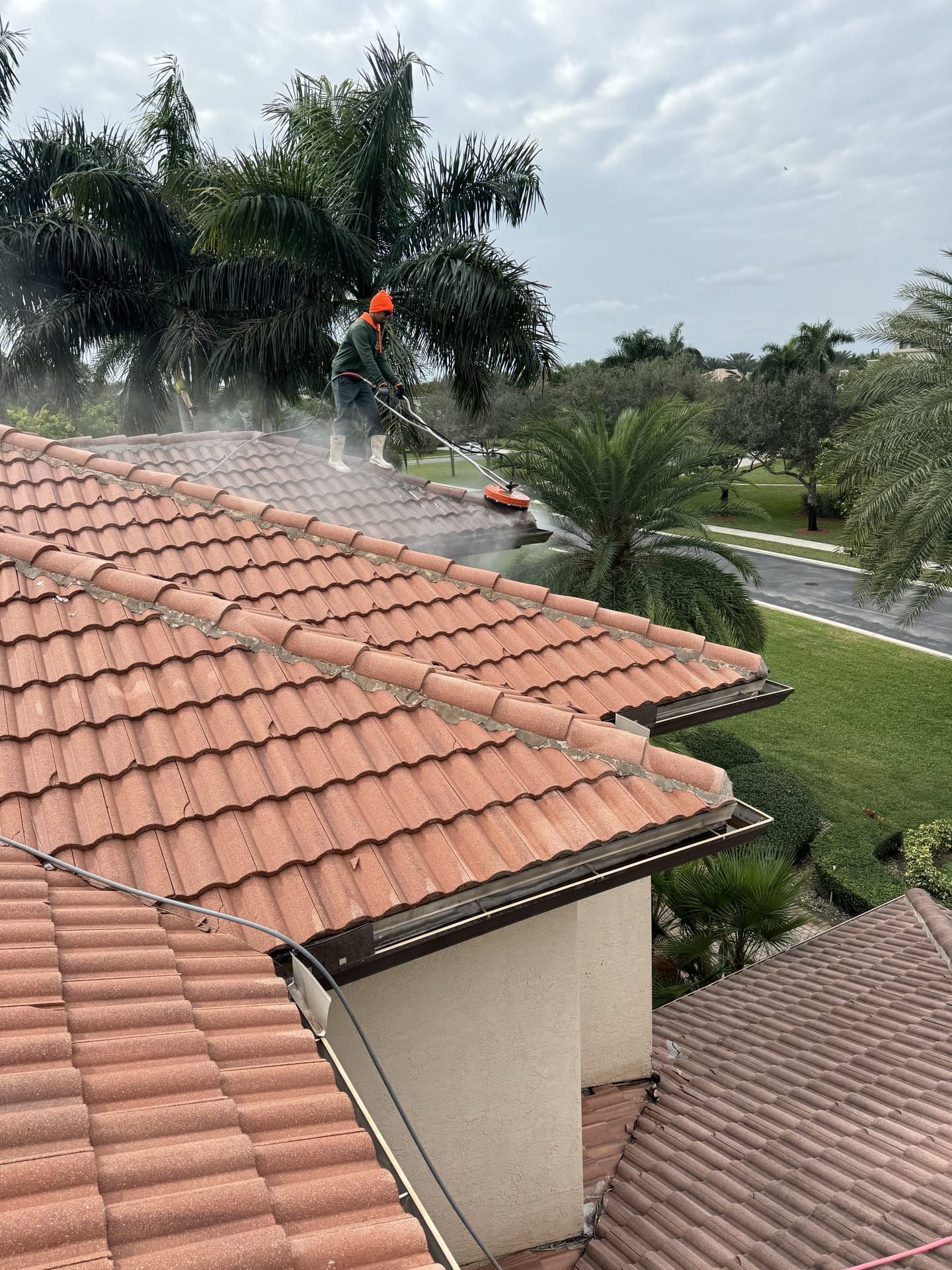 Soft wash spray lifting grime from a barrel-tile roof